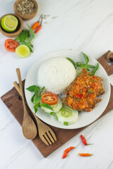 Ayam geprek, Indonesian popular streed food, made from crispy chicken smashed with sambal or chili sauce, eat with rice and cucumber, lettuce, tomato and kemangi. Isolated background, copy space.
