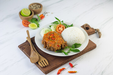 Ayam geprek, Indonesian popular streed food, made from crispy chicken smashed with sambal or chili sauce, eat with rice and cucumber, lettuce, tomato and kemangi. Isolated background, copy space.