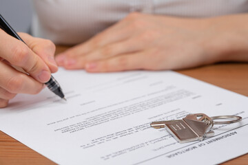 Close-up view of estate broker agent signing mortgage application form with house key. Concept of buying new house.