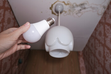 Female hand holding a led light bulb to change, replace it at home, screwing in the bulb into a lamp holder for energy saving and economy, saving money