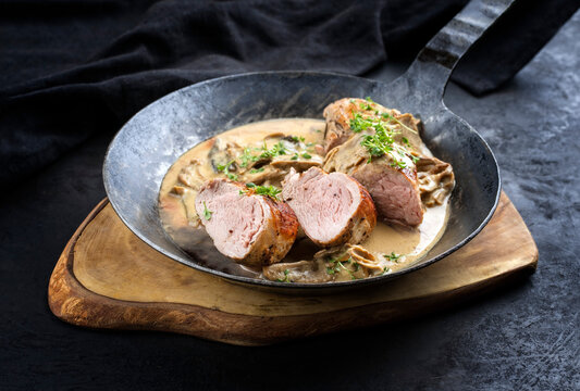 Traditionelle gebratene iberische Filet Medaillons vom Schwein in Rahmsauce mit Pilzen und Kr&auml;uter angeboten als close-up in einer rustikalen schmiedeeisernen Pfanne auf einem Holz Board