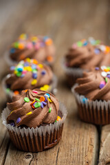 Close-up view of tasty chocolate cupcakes with colored sprinkles on rustic wooden table background. Sweet dessert. Bakery concept. Elegant food. Sweets for coffee or tea.