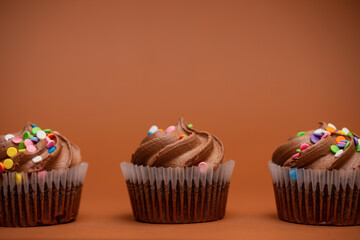Brown cupcakes with chocolate cream and colored sprinkles on beige background. Sweet dessert. Bakery concept. Elegant food. Sweets for coffee or tea.