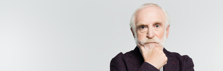 Pensive senior man in jacket looking at camera isolated on grey, banner