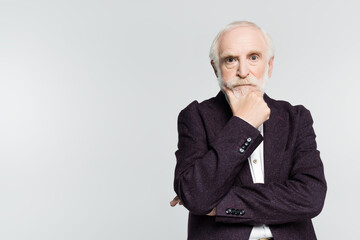 Thoughtful senior man in jacket looking at camera isolated on grey