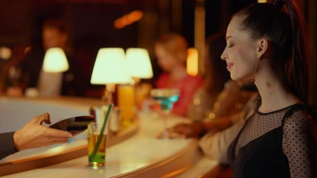 Gorgeous woman buying cocktail in nightclub. Barman giving woman bank terminal