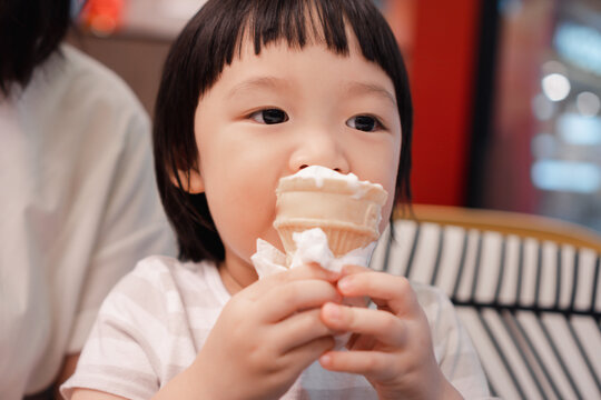 Asian 3 year old girl with  face eat ice cream cone. Concept for  sweet food and family life.