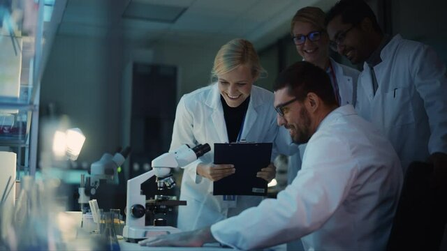 Surprized Male Reseach Scientist Makes an Important Discovery While Researching Samples Under the Microscope. Happy Colleagues Give High Five and Share Success with Fellow Bioengineers.