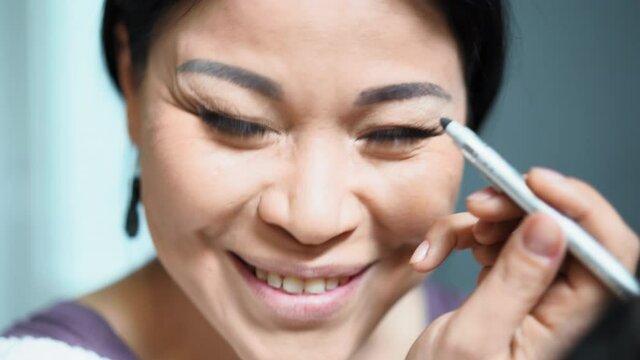 Middle-aged woman paints her eyebrow with a pencil. Asian draws the shape of her eyebrows herself. High quality 4k footage.