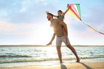 Happy father and his child playing with kite on beach near sea. Spending time in nature