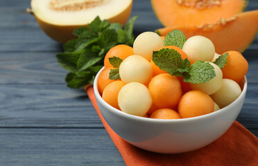 Melon balls and mint in bowl on blue wooden table, closeup. Space for text