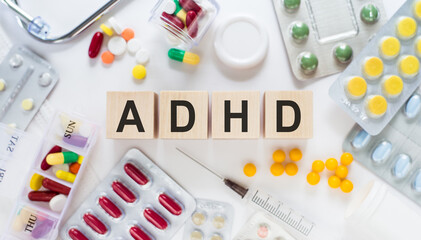 Abbreviation on ADHD (Attention Deficit Hyperactivity Disorder) cubes on wooden blocks on the table. Medical concept with pills, vitamins, stethoscope and syringe in the background.