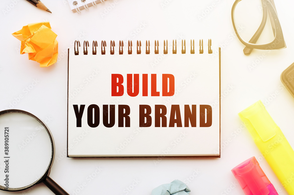Fototapete build your brand - text written in a notebook against the background of stationery tools.