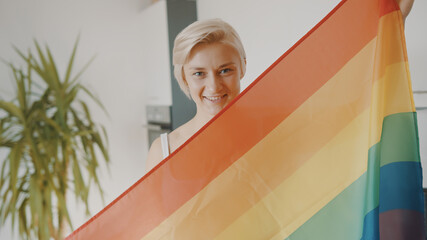 Young blond woman with rainbow flag in her appartment. High quality photo