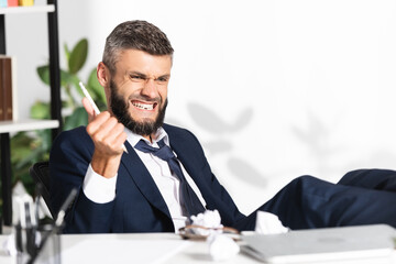 Naklejka premium Nervous businessman holding pencil near clumped paper and laptop on blurred foreground in office