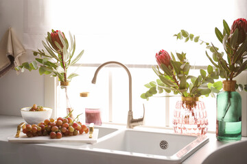 Vases with beautiful protea flowers near sink in kitchen. Interior design
