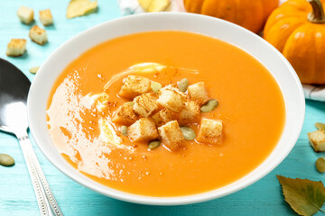 Tasty creamy pumpkin soup with croutons and seeds in bowl on light blue wooden table, closeup