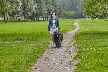 White woman walks with black briard in facial mask on open air.