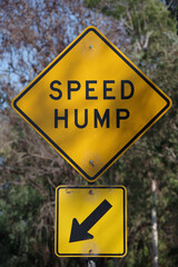 Close-up view of a yellow and black traffic sign SPEED HUMP and and arrow sign pointing at that location