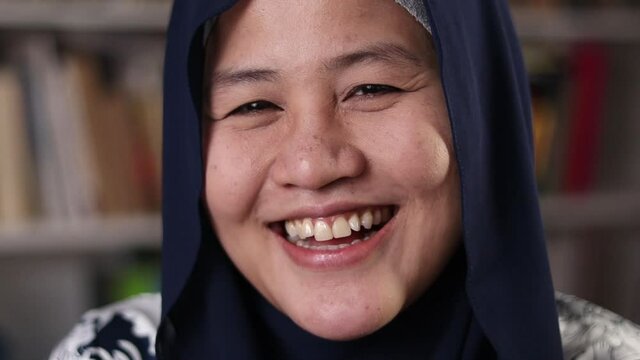 Happy Asian muslim woman wearing hijab smiling and laughing to camera, female student in library