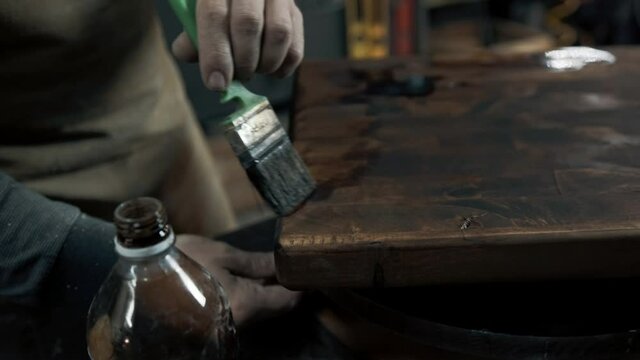A carpenter paints a piece of wood for a loft-style chair with a brush. Close up