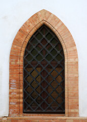 Fototapeta premium pointed windows with grille and glass, decorated with bricks around the arch on a white facade of a gothic building- elvish style of architecture