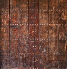 ancient and worn medieval double door gate with rivets on a rough wooden texture surface - epic weathered background