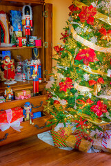 Nutcrackers and Santas stand among presents in a cabinet next to a  Christmas tree.