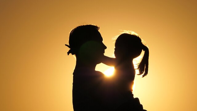 daddy is circling his beloved healthy daughter in his arms. silhouette of dad and child at sunset. happy father and little child hugging in the park on nature in rays of sun. family on vacation.