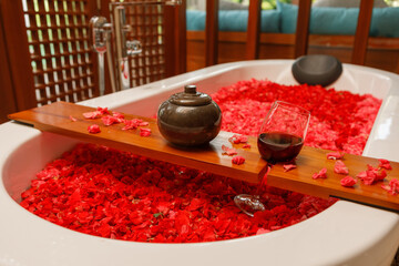 Glass of red wine beside bathtub with flower petals, top view from above. Surprise for valentines day