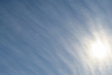 Sun behind long wispy clouds against a blue sky, as a nature background
