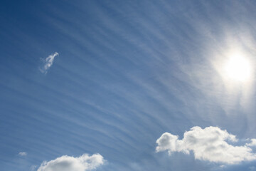 Sun behind long wispy clouds against a blue sky, as a nature background
