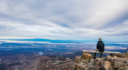 Adventurous man sitting on top of a bench looking at the open landscape on a cloudy day.