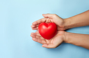 Adult hand holding red heart on light blue background