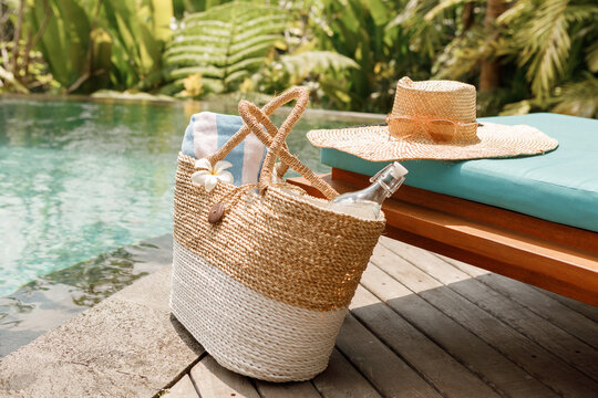 Summer beach bag with straw hat,towel,sunglasses and bottle of water near swimming pool