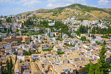 Panoramic view on Granada city suburbs and mountains on horizon from the castle, Spain. A picturesque mixture of historic and modern urban architecture under a blue sky. - 389121958