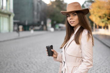 stylish woman of European appearance stands on the street and drinks coffee from disposable tableware.