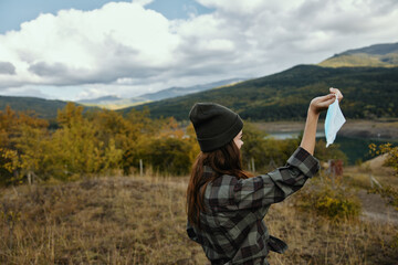 A woman holds a medical mask in her hand in the autumn forest and mountains in the background