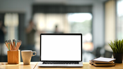 Front view of designer creative work space with blank screen laptop on wooden table and blurred interior of modern office background.