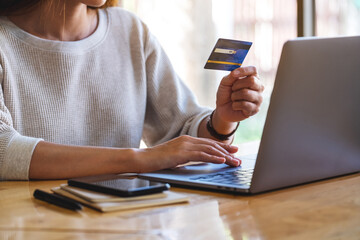 Closeup image of a woman holding credit cards while using laptop computer in office