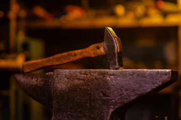 A blacksmith's hammer lying on an anvil in a dark forge. Blacksmithing tools
