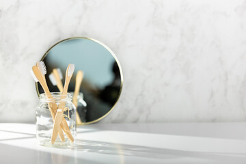 Bamboo toothbrushes and mirror in glass near white marble wall in bathroom