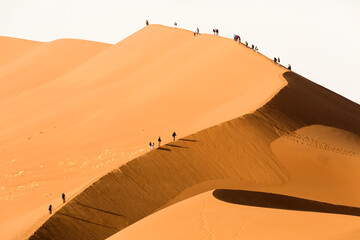 Tourists climbing a large red sand dune in Sossusvlei, Namibia.