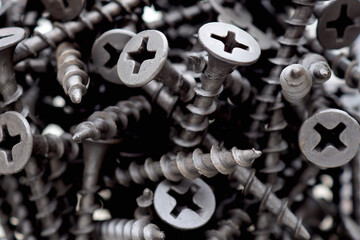 Lots of black self-tapping screws close up. A bunch of hardware. Fasteners and materials for construction and repair. Dark black and white manufacturing industrial illustration. Macro