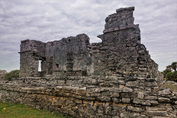 Fototapeta na wymiar Ruins of the ancient Mayan city of Tulum. A dilapidated stone building rises against a cloudy sky. Memory of a bygone civilization. Mexico.