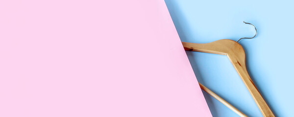 Empty wooden clothes hanger on pastel pink and blue background with copy space. Sale and shopping concept. Banner.