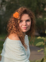 A portrait of young russian siberian beautiful girl is sitting outside with an orange flower in red hair.