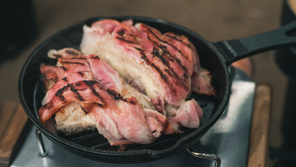 Quick tasty snack.Bread wrapped in bacon and cheese between them fry on a iron pan in camping outdoor cooking.