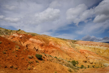 Martian landscape, natural landmark of Altai Republic. Mountains colored red, yellow, and orange against a blue sky with white clouds.