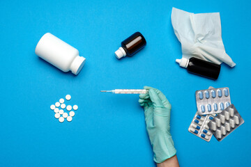 doctor in latex gloves holding Mercury thermometer over blue background with pills